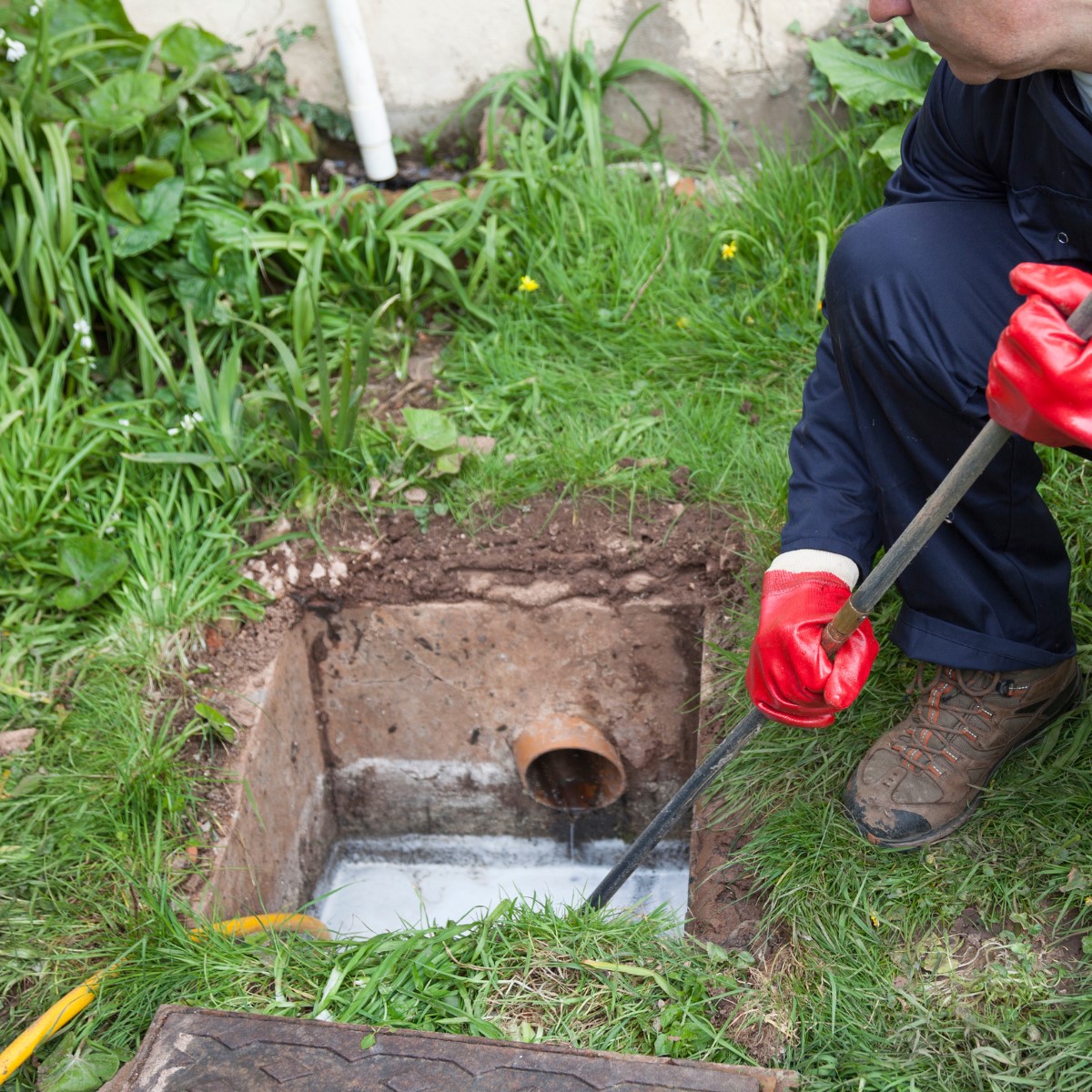 Drainage engineer using drain rods to clear a blocked underground drain through an inspection chamber.