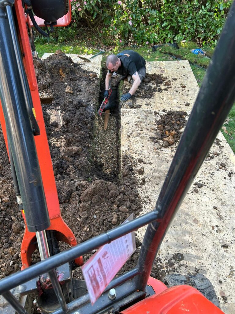 Engineer carrying out emergency drain excavation and repair work on a damaged underground drainage pipe.