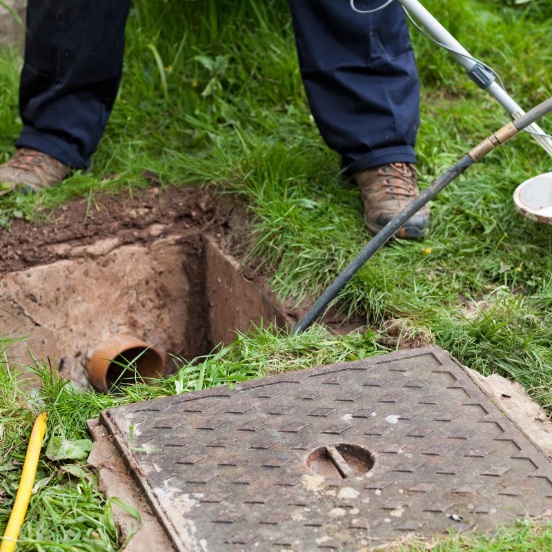 Drainage engineer clearing a blocked underground drain through an inspection chamber using professional drain rods.