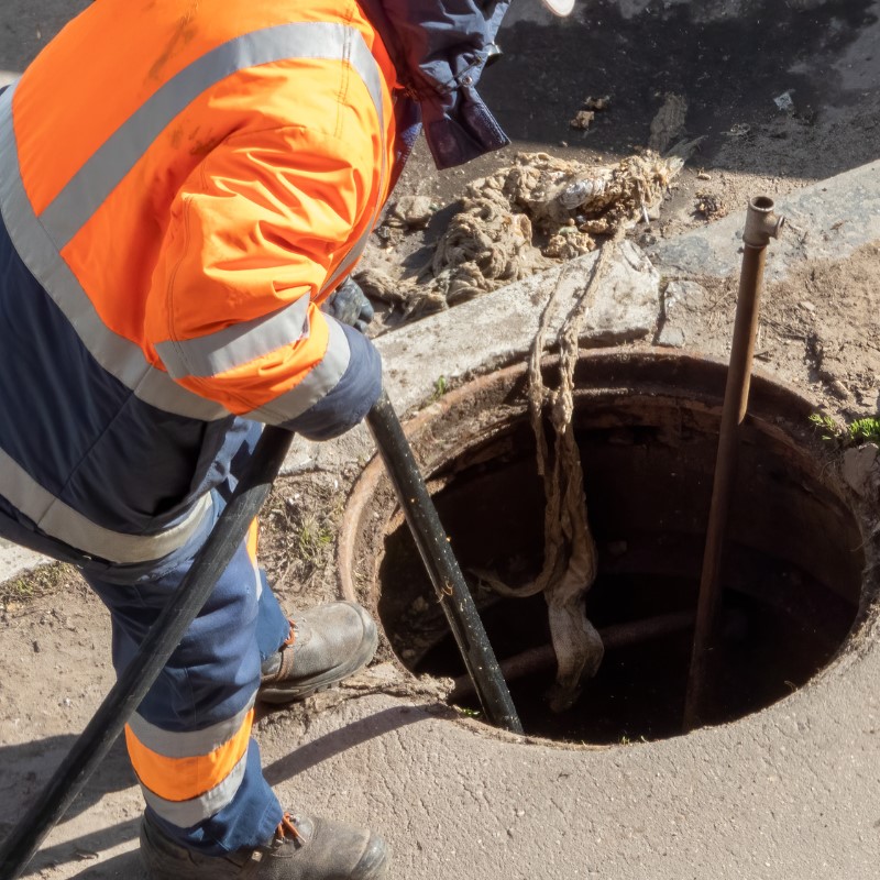 Drainage engineer carrying out drain repair work through an inspection chamber to restore a damaged drainage system.
