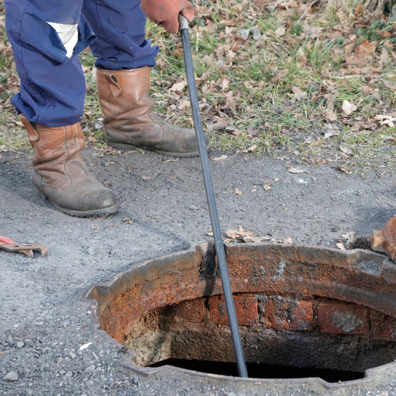 Drainage engineer using drain rods to clear a blocked drain through an inspection chamber.