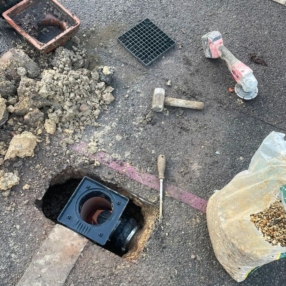Exposed drainage gully with a loose grate and tools on the surrounding paved surface