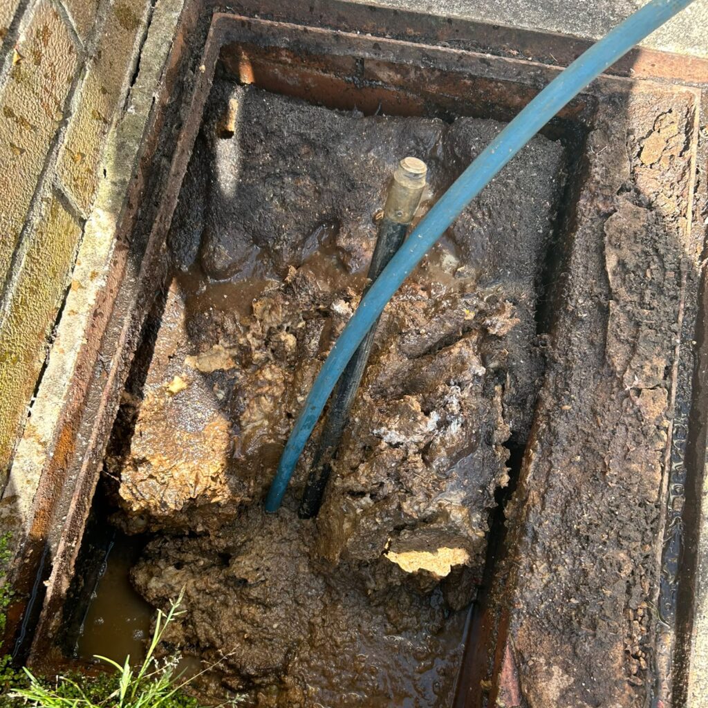 Blue drain-cleaning hose inside an open brick inspection chamber