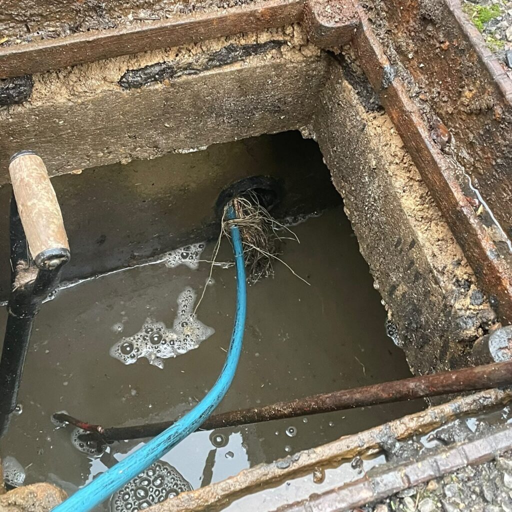 Blue drain-cleaning hose entering an open inspection chamber