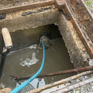 Blue drain-cleaning hose entering an open inspection chamber